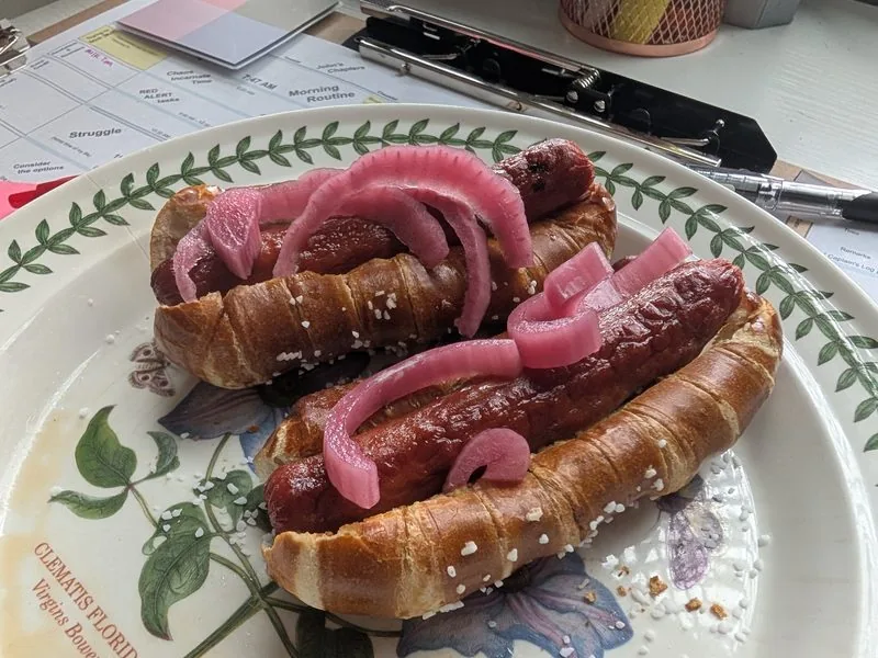 Sausage in a pretzel bun topped with our pickled red onions